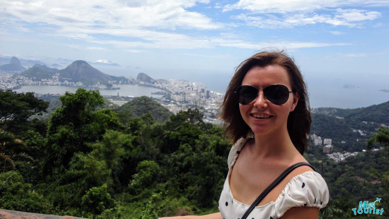 The writer of the article stands in front of a scenic overlook with a panoramic view of Rio de Janeiro's mountains and cityscape