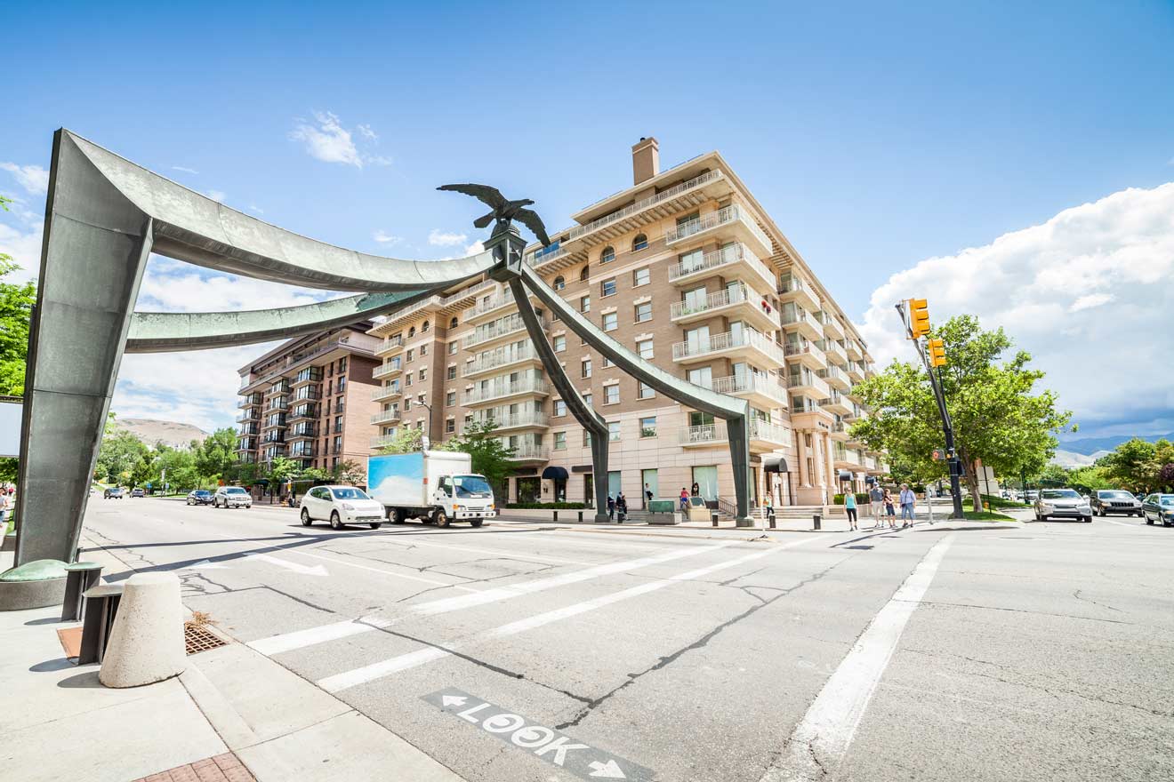 Street view of an intersection with a sculpture featuring an eagle. Vehicles and pedestrians are present, and a multi-story building is visible in the background under a clear sky.