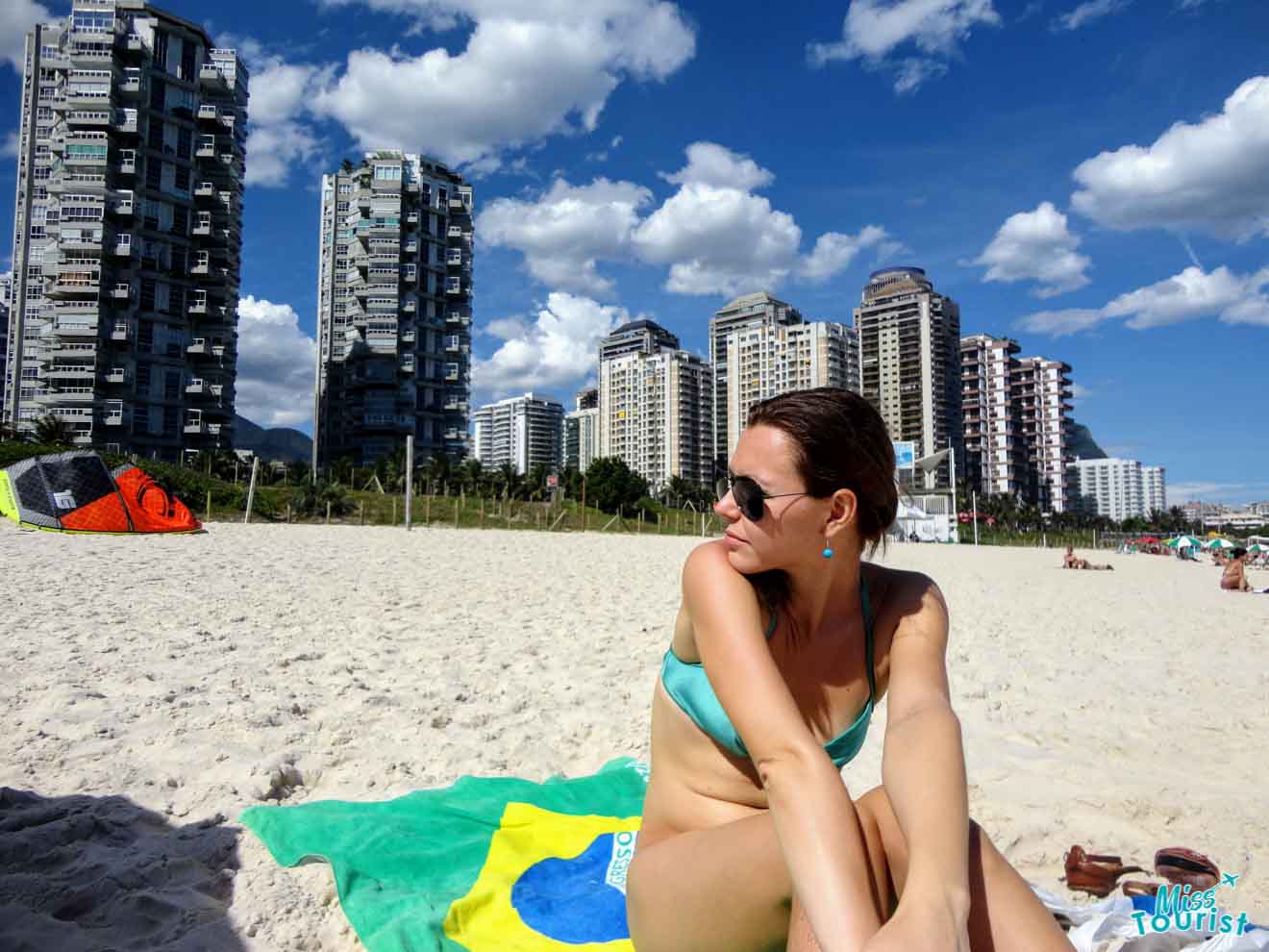 The writer of the post lounging on the beach with a Brazilian flag towel, with Rio de Janeiro's distinctive skyline and beachgoers in the background