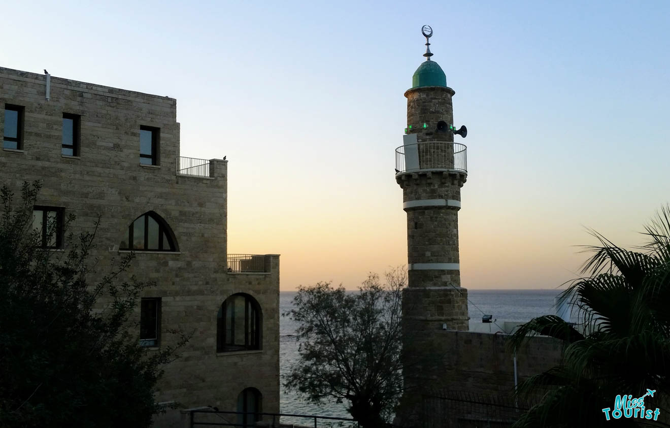 Close-up view of an ancient stone minaret with a green dome against a twilight sky, seen from a distance.