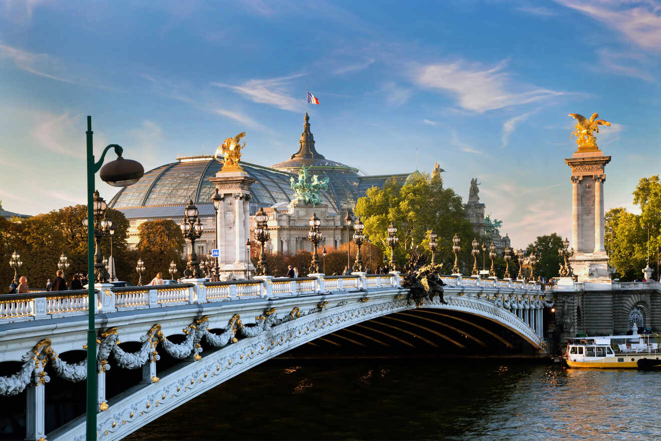 The image shows the ornate Pont Alexandre III bridge in Paris with the Grand Palais in the background, under a clear blue sky.