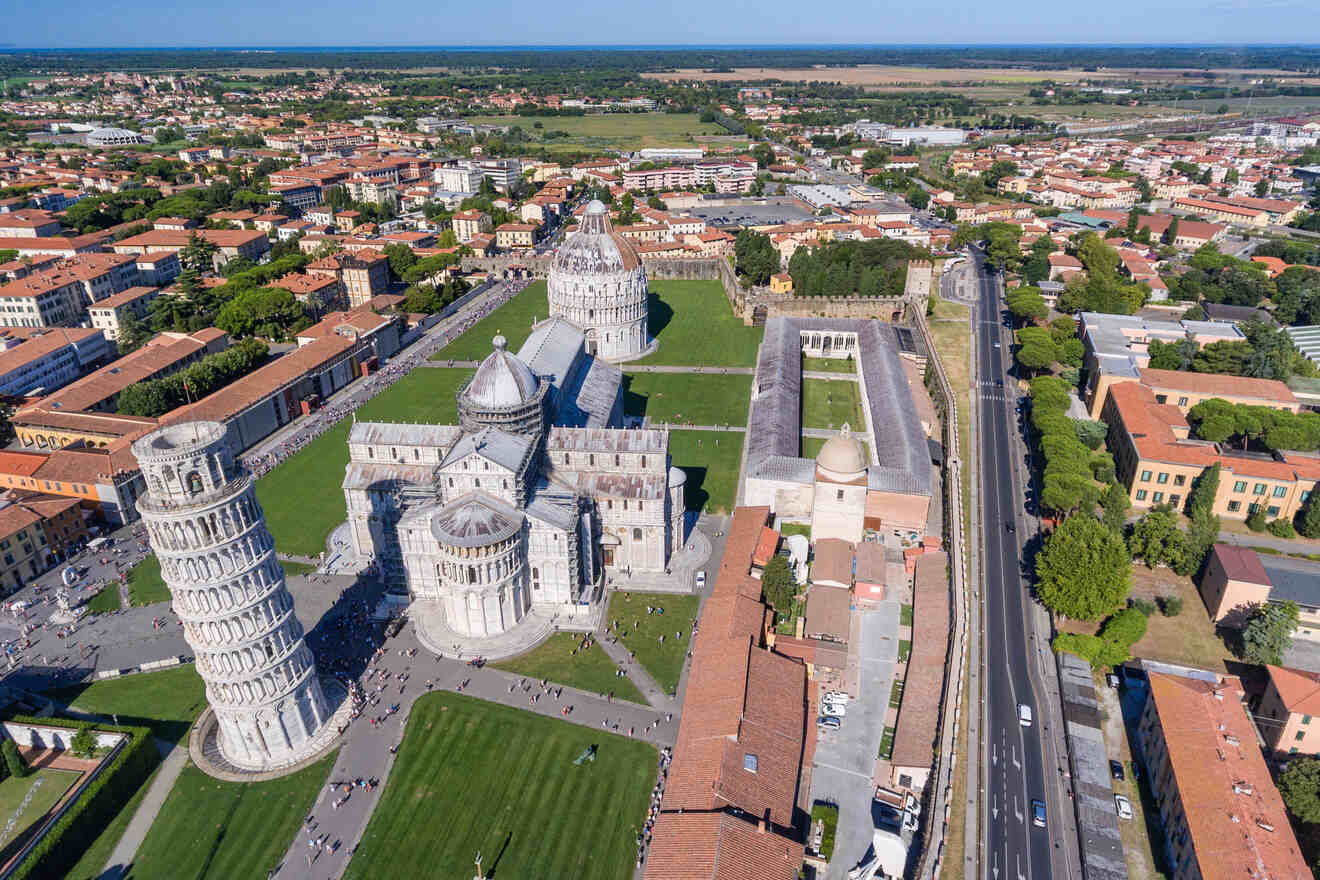 Aerial view of the Leaning Tower of Pisa, Cathedral of Pisa, and the Baptistery of St. John in Pisa, Italy, surrounded by green lawns and city buildings.
