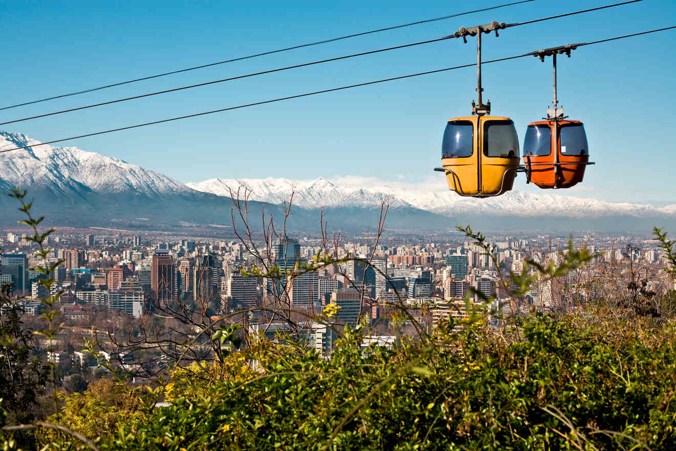 Two colorful cable cars suspended over Santiago de Chile, with the cityscape and Andes Mountains in the background.