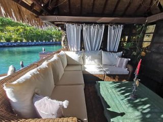 A cozy outdoor seating area with a white cushioned sofa and a view of the water, under a thatched roof.