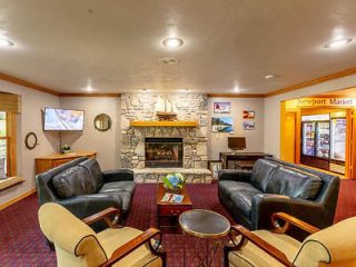 A cozy hotel lobby with leather sofas, armchairs, a stone fireplace, framed nautical pictures, a flat-screen TV, and a small market area to the right.