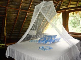  A rustic bedroom with a bed covered by a white mosquito net, set under a thatched roof.