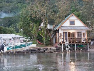 A charming lakeside cottage with a small boat docked nearby, surrounded by lush trees.