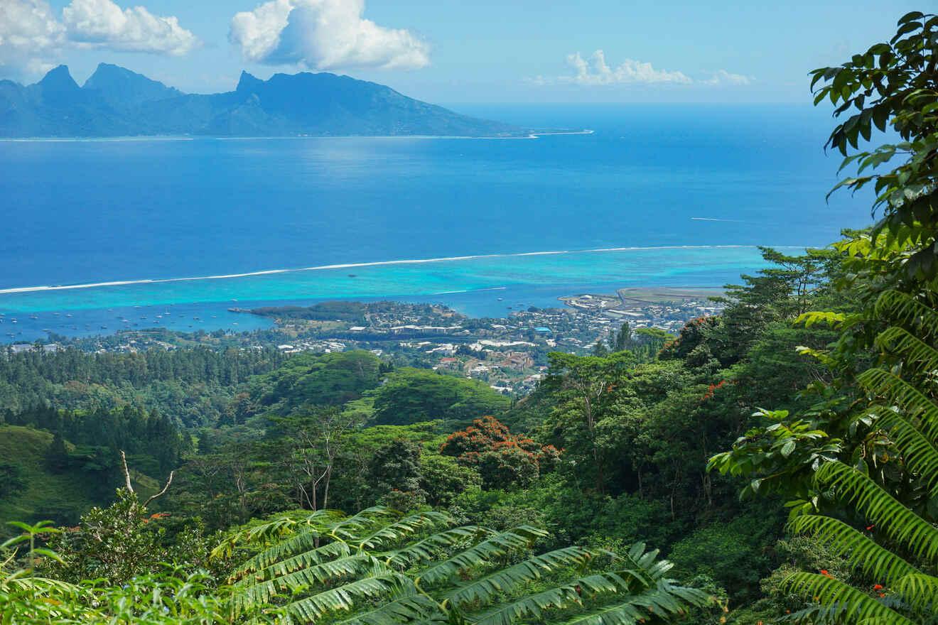 Stunning aerial view of a coastal town with turquoise waters, green forests, and distant mountains in Tahiti