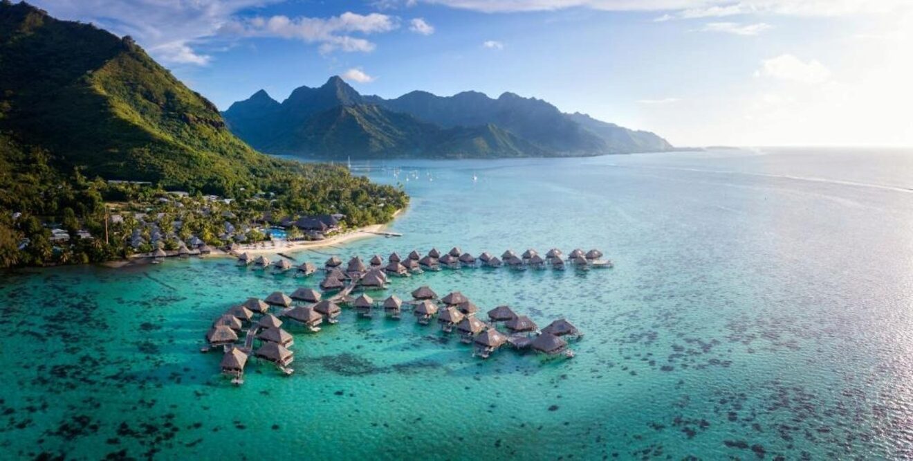 Overwater bungalows in a serene, turquoise lagoon with lush green mountains in the background in Tahiti