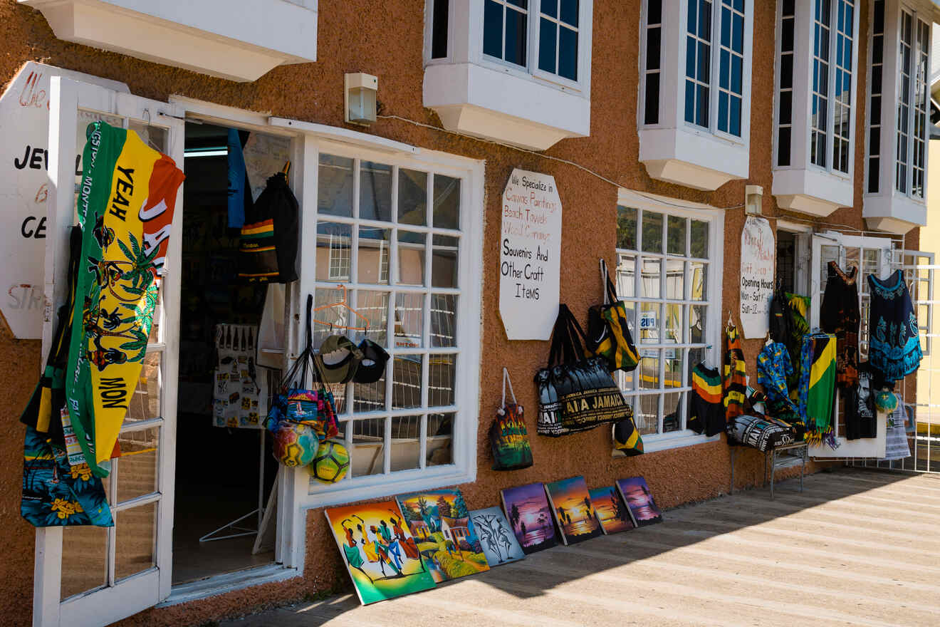 Shop with open glass doors displays colorful bags, beach towels, and paintings. Signs advertise jewelry and crafts.