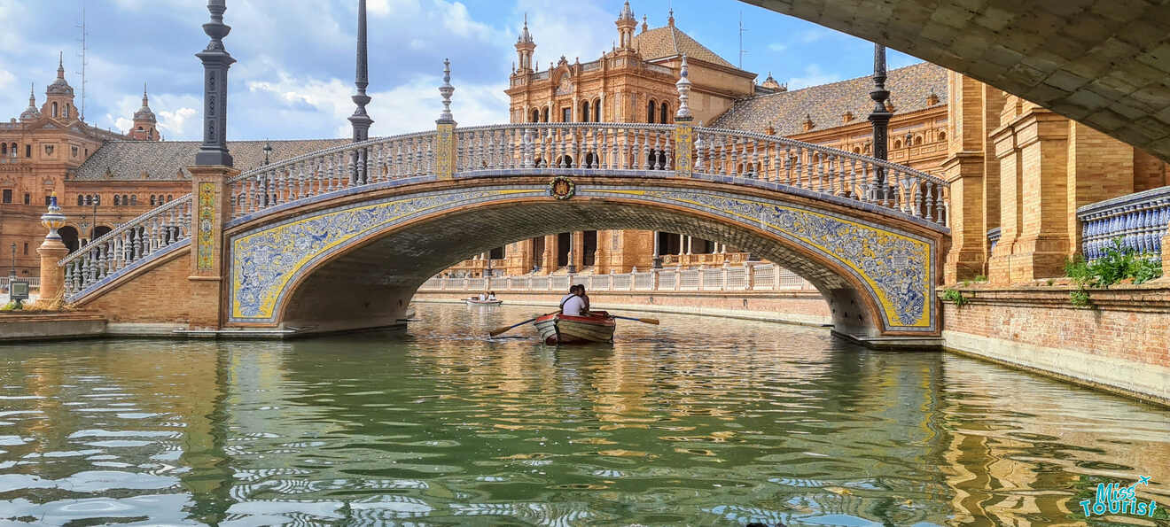 A serene moment captured as a person rows a boat under a beautifully tiled bridge at Plaza de España in Seville, showcasing the intricate architecture and calm waterways