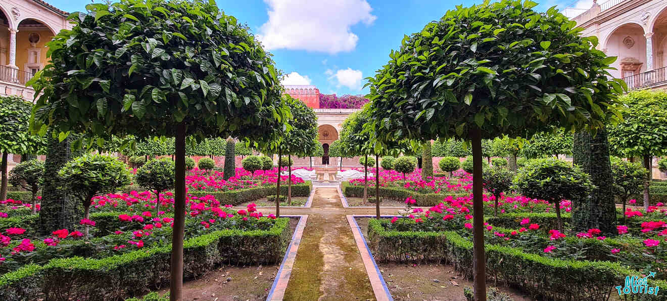 A serene and meticulously manicured garden path lined with vibrant pink flowers and neatly trimmed hedges, leading to a classic fountain and elegant architectural facade under a bright blue sky.