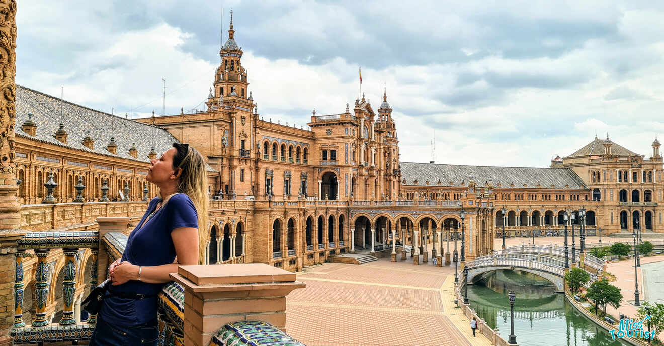 A visitor basks in the grandeur of Plaza de España in Seville, her gaze uplifted to admire the intricate Renaissance Revival architecture, with the expansive building's wings embracing the open square and bridge