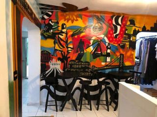 A colorful mural covers the wall of a small indoor cafe with wooden tables and chairs. A clothing rack with hanging clothes is visible on the right.