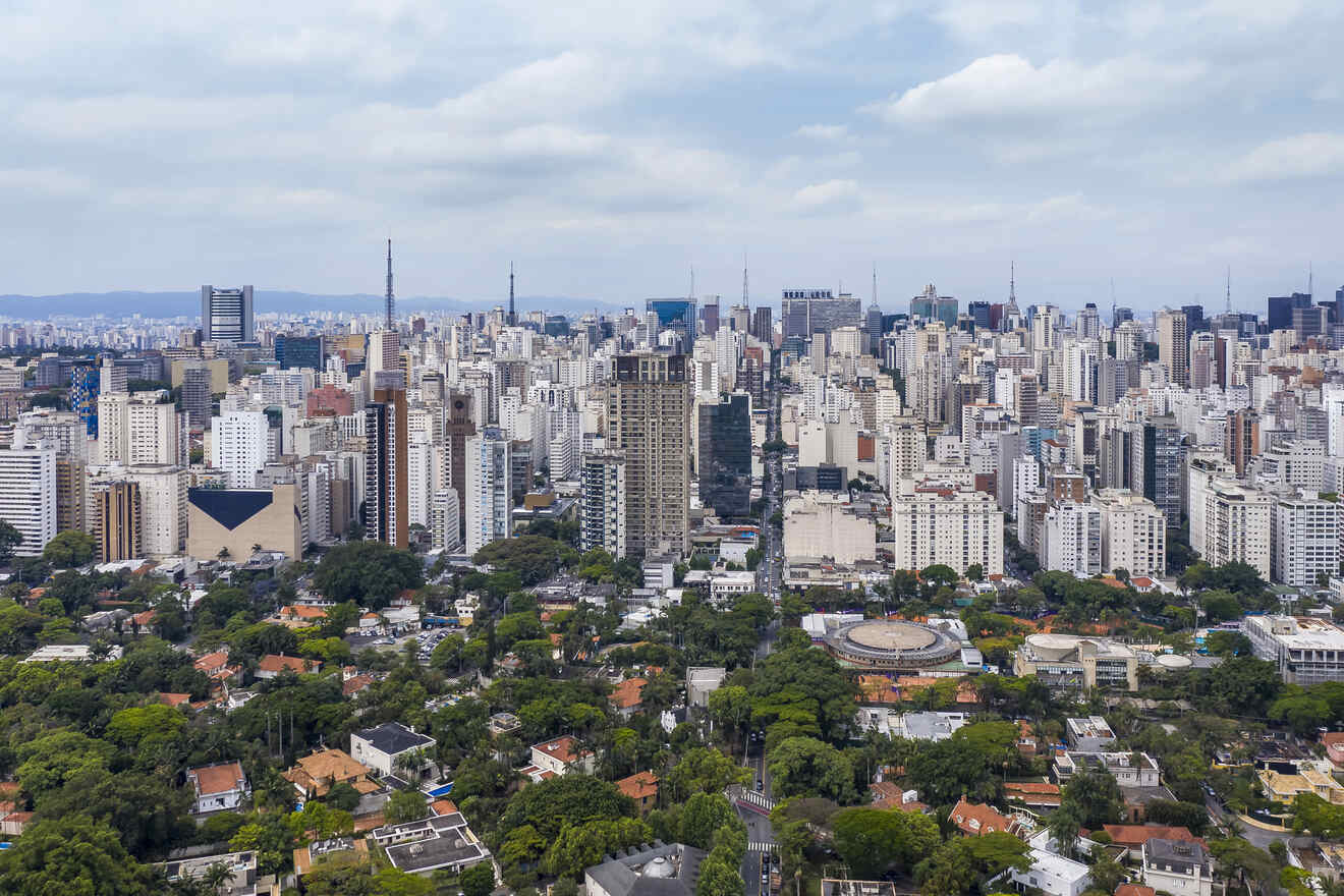 Aerial view of a sprawling urban area with a mix of tall buildings and residential houses surrounded by greenery under a cloudy sky.