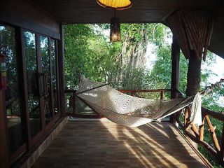 A cozy hammock on a wooden balcony surrounded by lush greenery.