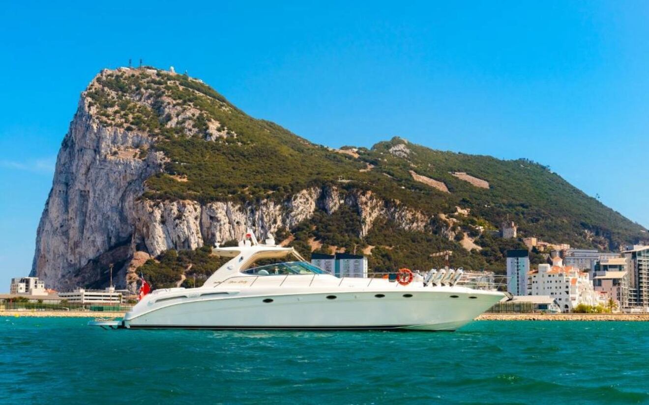 A white yacht is anchored in the water with the Rock of Gibraltar in the background under a clear blue sky.