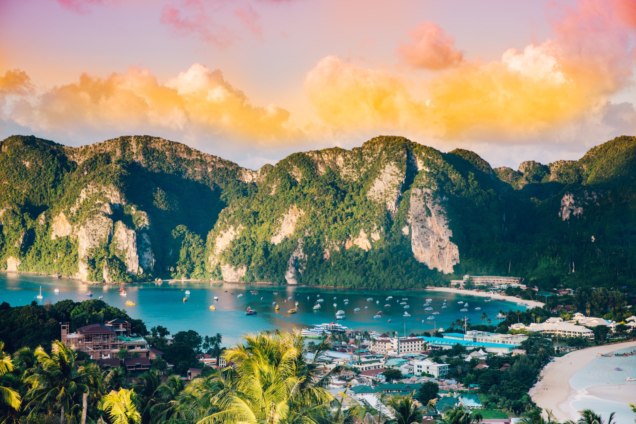 A stunning sunset view of a coastal town nestled between green mountains and blue waters.