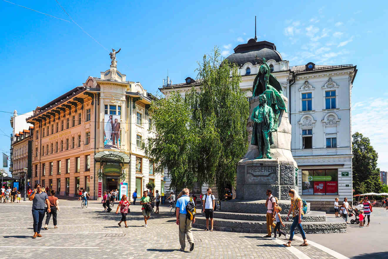 People walking around a public plaza with a large statue in the center, surrounded by historic buildings under a clear blue sky.