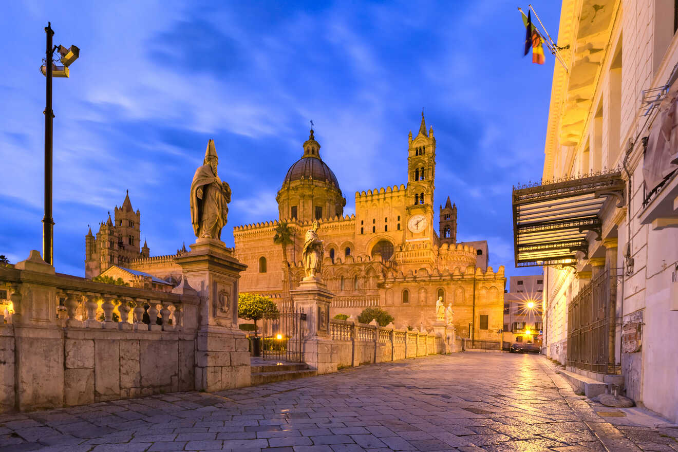 Evening view of Palermo Cathedral with illuminated statues and historic architecture under a blue sky.