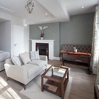 Open-plan studio at Beech House Apartments, with a cream sofa facing a fireplace, wooden coffee table, upright piano