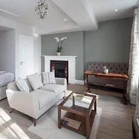 Open-plan studio at Beech House Apartments, with a cream sofa facing a fireplace, wooden coffee table, upright piano