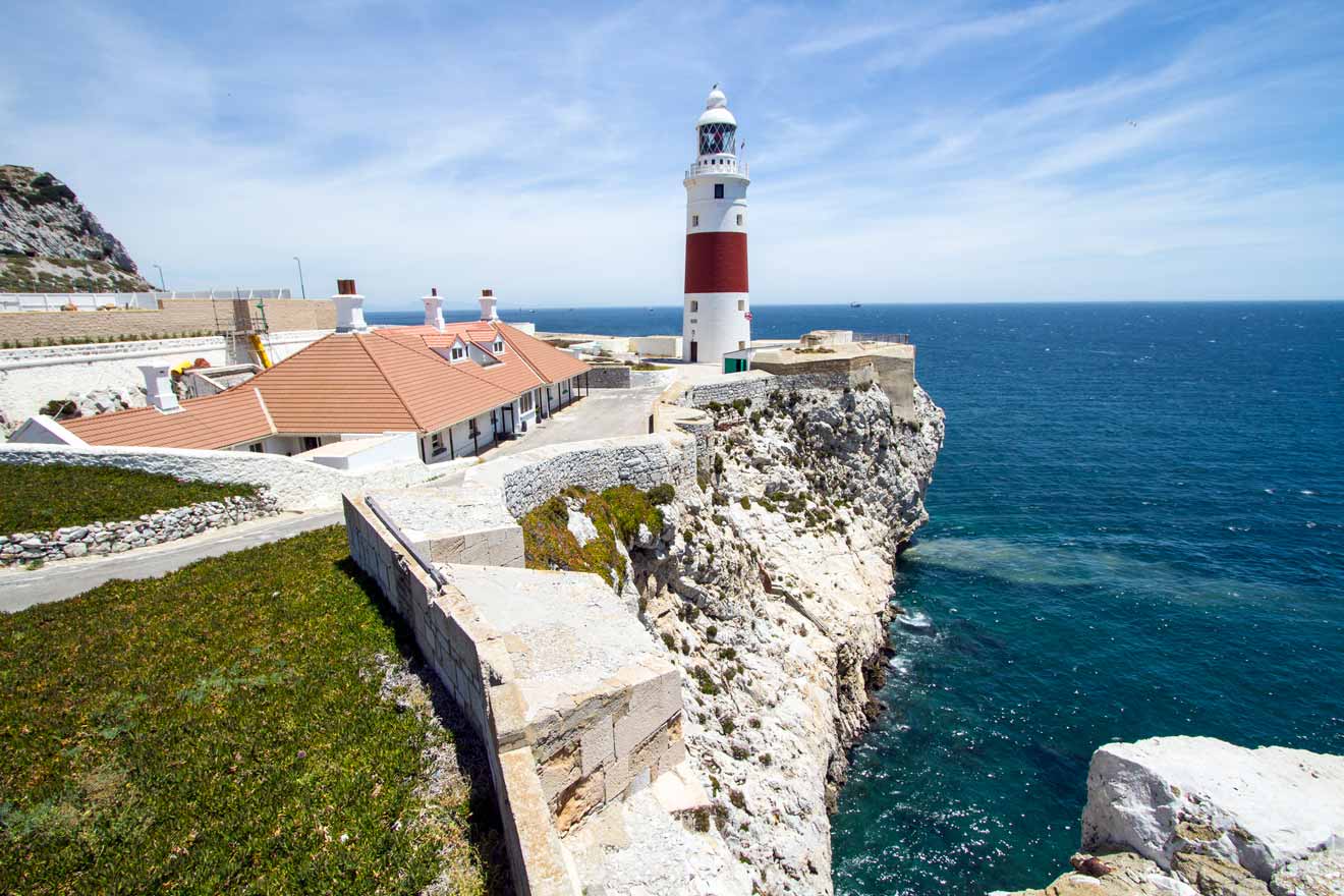 Lighthouse on a rocky cliff by the sea under a clear blue sky.