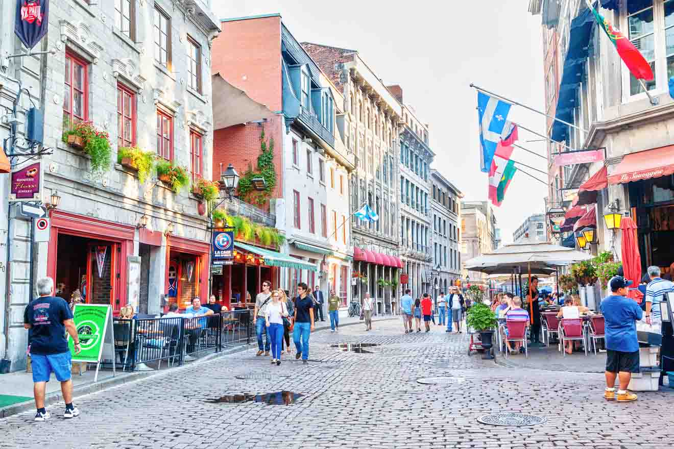A bustling Montreal old town street scene with pedestrians, colorful flags, and quaint buildings housing restaurants and shops
