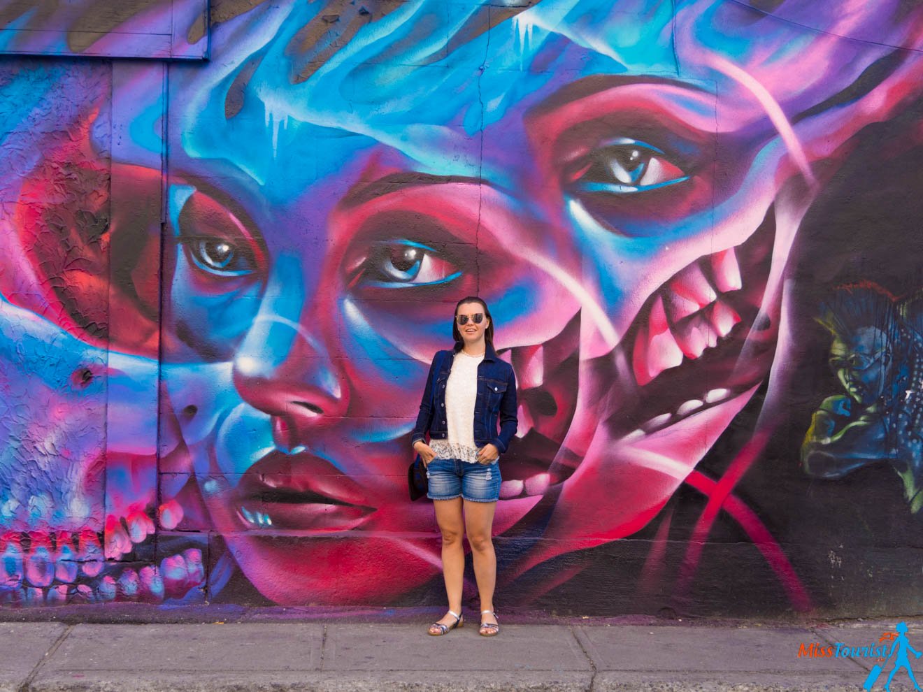 The writer of the post, Yulia,  standing in front of a vivid street mural featuring intense blue and red hues, and a portrait of a woman's face.