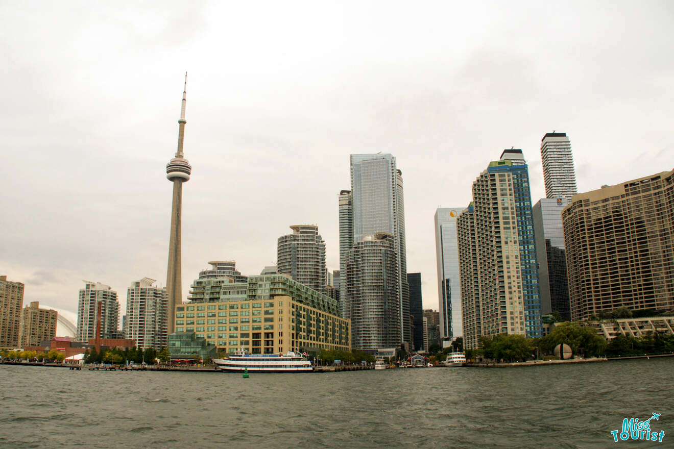 Overcast skyline of Toronto from the harbor, featuring the iconic CN Tower and modern skyscrapers reflecting on the water's surface