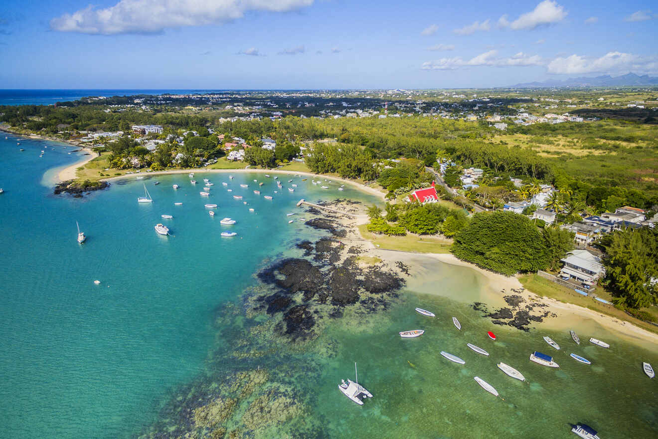 Aerial shot of view of Grand Bay, a peaceful bay dotted with numerous sailboats anchored in the calm blue waters near a sandy beach, with a vibrant landscape and clear skies in the background