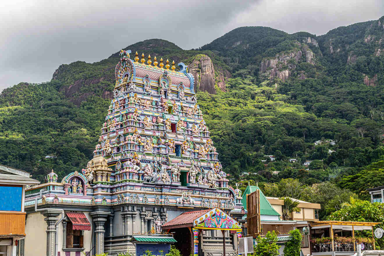 An ornate, colorful temple set against a backdrop of lush green mountains, with intricate carvings and statues adorning its facade.