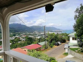 A view from a balcony overlooking a residential neighborhood with houses, greenery, and mountains in the background.