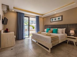Elegant hotel room with a plush bed, aqua accent pillows, and sliding doors to a sunny balcony