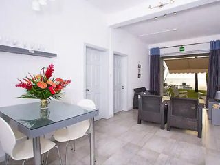 Modern dining area with white chairs, glass table, bright red flowers, leading to a furnished patio