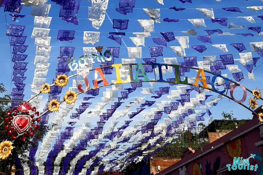 Colorful banners and sunflowers decorate an archway with the words "Barrio Jalatlaco" against a blue sky.