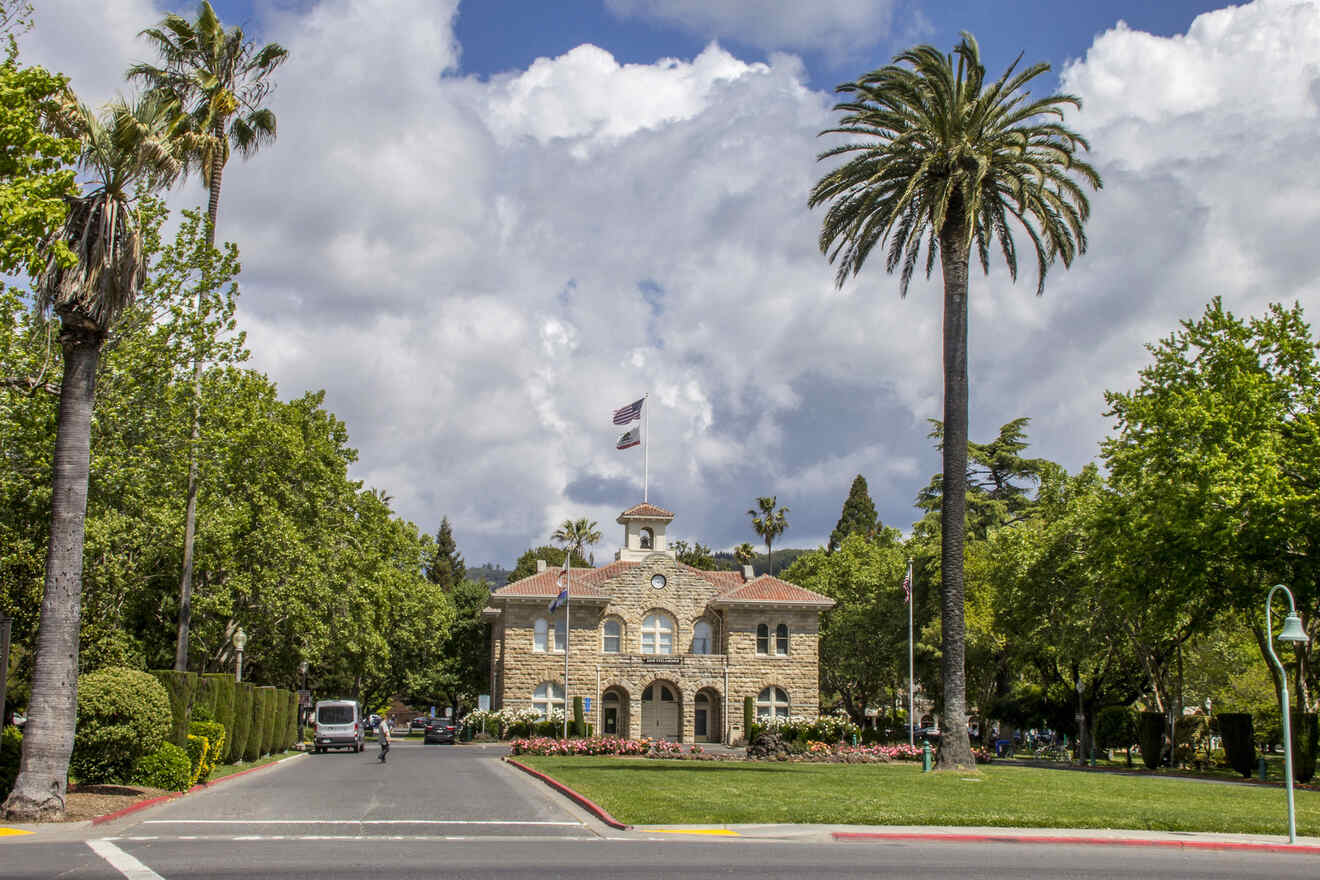 A historic building with a clock tower and American flags, surrounded by lush greenery and palm trees.