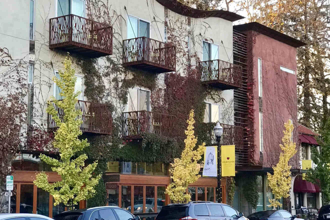 A modern building with balconies covered in ivy and a few cars parked in front.