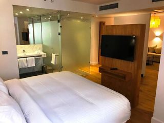 Modern hotel room with a glass-walled bathroom and a flat-screen TV.