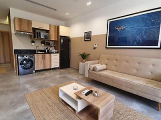 Contemporary studio apartment with a beige couch, kitchenette, and laundry appliances.