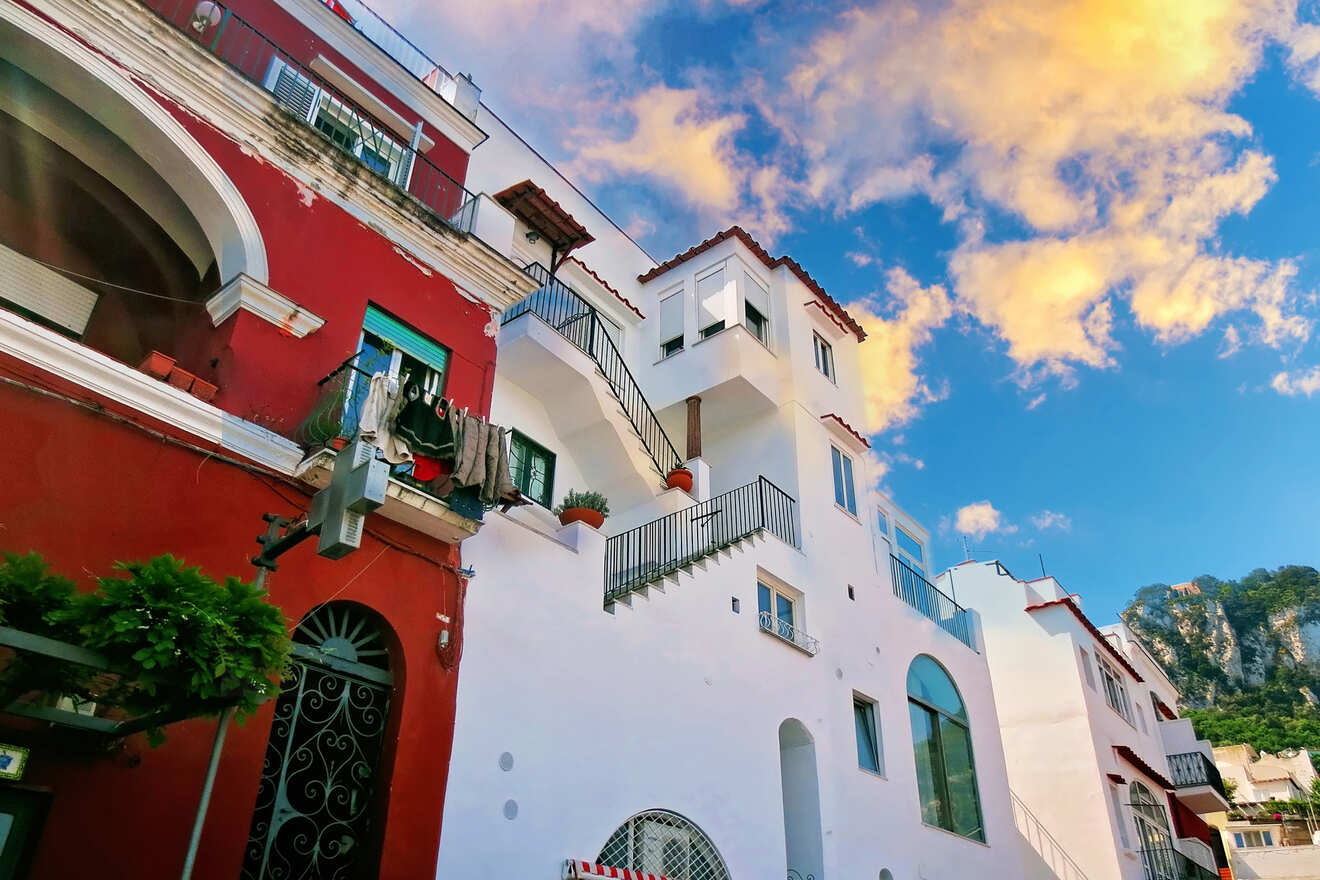 A multi-story building with red and white facades stands under a blue sky with scattered clouds. Clothes hang on a line from a balcony on the red section of the building.