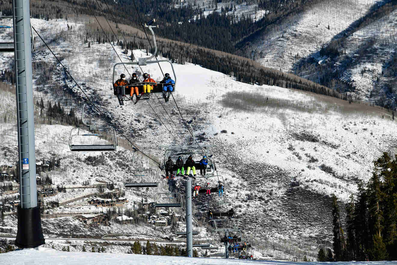 Skiers on a chairlift ascending over a snowy mountain slope with a view of ski trails and forested areas in Vail, Colorado