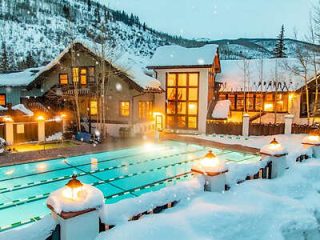 Illuminated outdoor pool surrounded by snow with glowing lights at a mountain resort during twilight