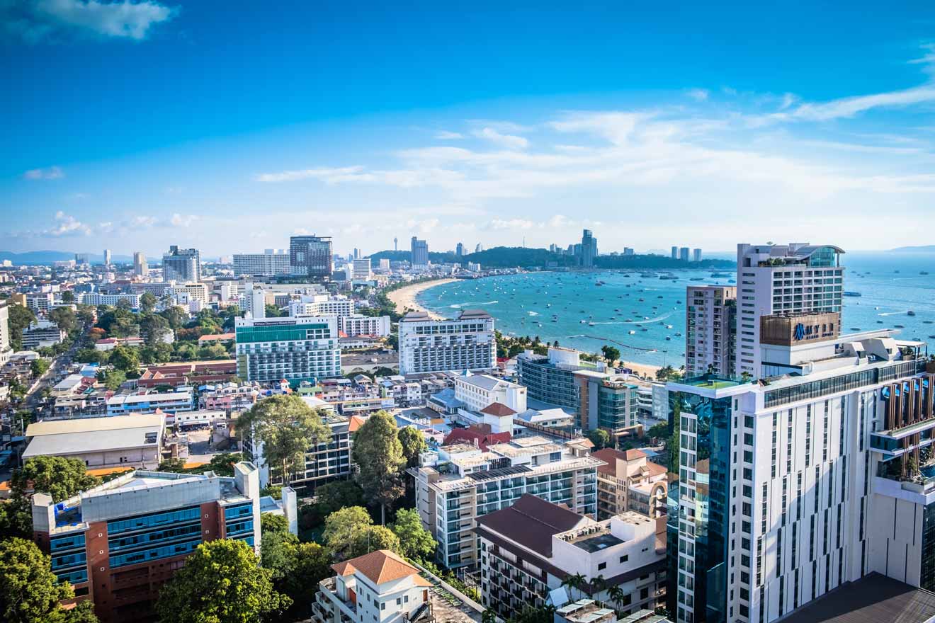 Aerial view of a coastal cityscape in Pattaya with modern buildings and a bustling bay filled with boats under a clear blue sky.