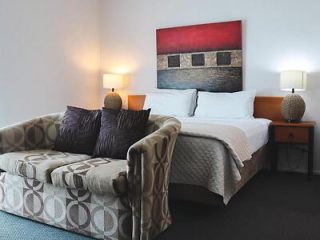 Stylish bedroom with a plush bed, geometric-patterned sofa, and an abstract red and grey wall painting