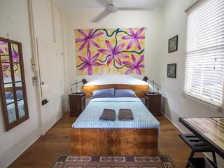 Rustic bedroom with a wooden bed, blue-striped bedding, and a large vibrant painting of flowers above the headboard