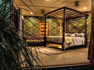 Exotic bedroom featuring a four-poster bed with elegant draping, surrounded by lush tropical plants and ambient lighting