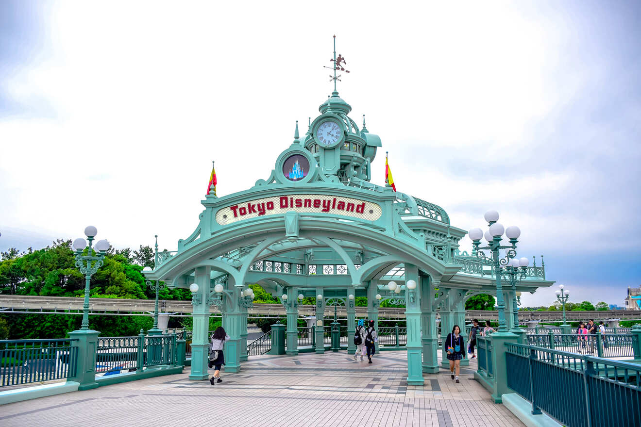 Entrance to Tokyo Disneyland featuring the iconic green and white vintage-style gateway, with visitors walking underneath on a sunny day