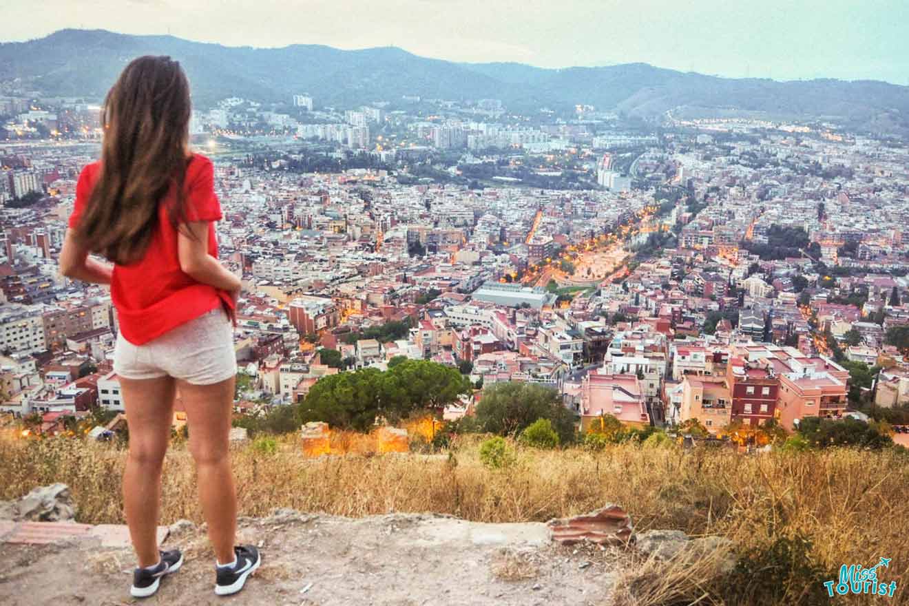 A girl is standing on a hill overlooking the city of barcelona.