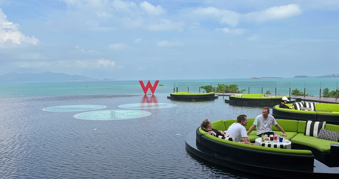 people sitting on booths in an infinity pool with a view of the sea